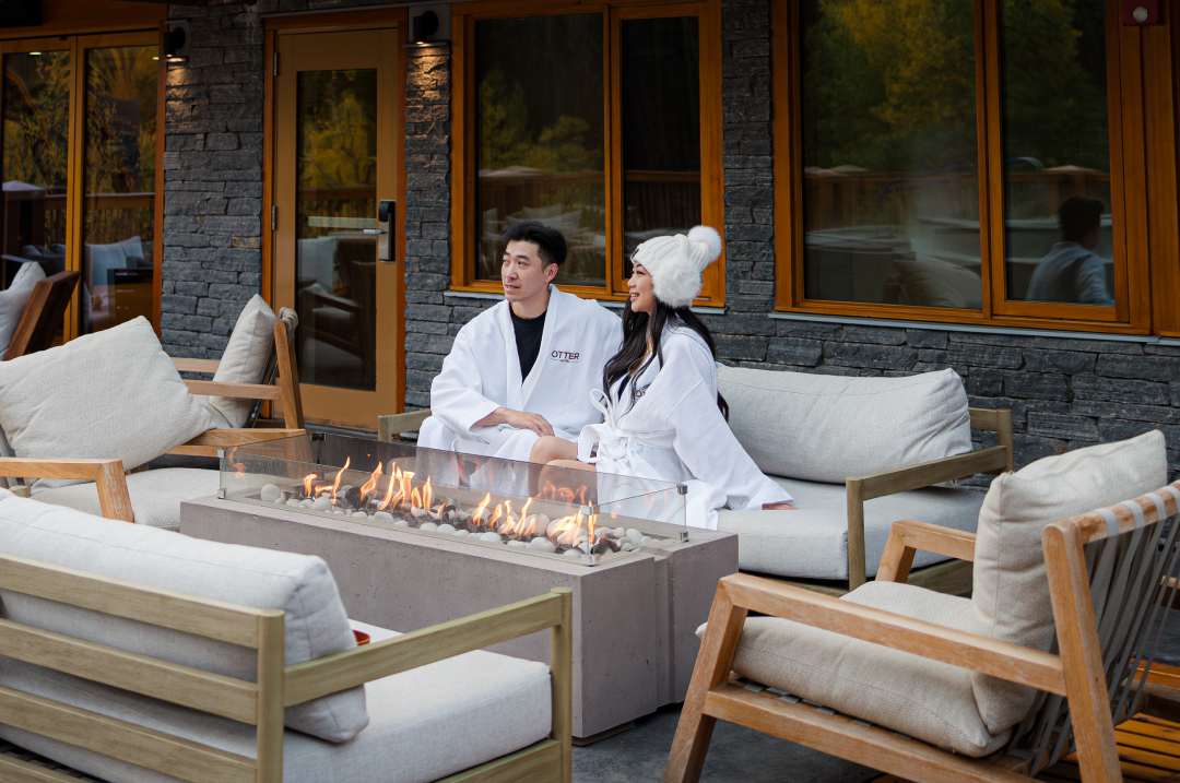 couple sitting by firepits on patio lounging in Otter hotel robes